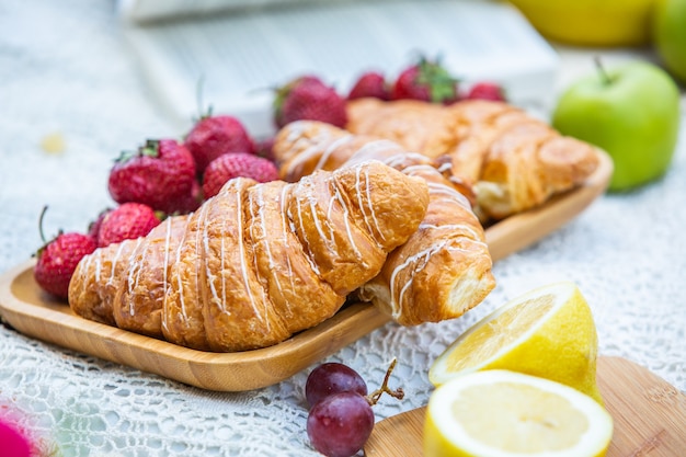 Picknick im Freien in einem üppigen grünen Park mit leckeren Croissantfrüchten, Donuts und Wein auf Gras