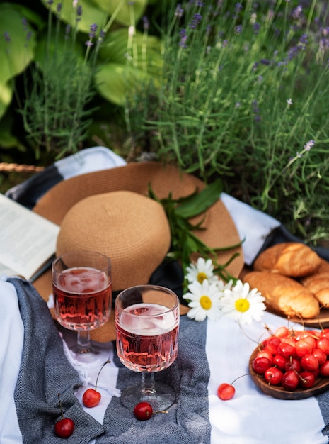 Picknick im Freien in Lavendelfeldern. Roséwein im Glas, Kirschen und Strohhut auf Decke