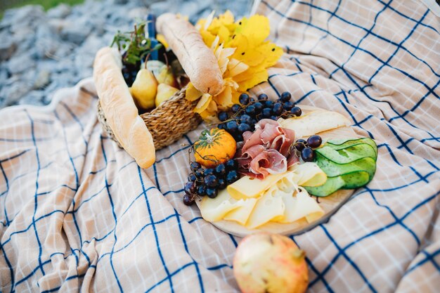 Picknick im Freien mit einem Teller Fleisch und Käse schneidet und Trauben einen Korb mit einem Baguette und einer Flasche