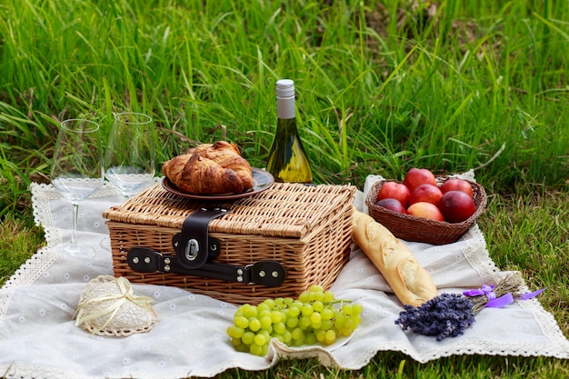 Picknick in der Natur: Tischdecke, Picknickkorb mit Geschirr, Baguette, Trauben, Pfirsiche