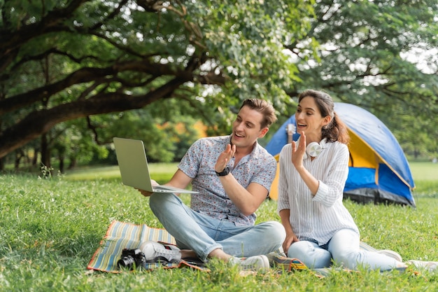 Picknick- und Campingzeit. Junge Paare, die Spaß haben, benutzen Laptop und Camping im Park. Liebe und Zärtlichkeit, romantischer Mann, der seiner Freundin Gitarre spielt, Lifestyle-Konzept
