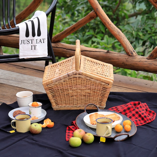 Picknickkorb mit Obst und Backwaren auf altem rustikalem Holztisch mit grüner Landschaft