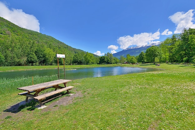 Picknicktisch aus Holz im Gras am Rande eines Sees in einem Freizeitpark in den französischen Alpen