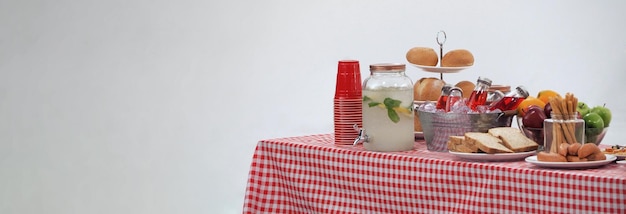 Picknicktisch und rot karierte Tischdecke mit Speisen und Getränken für Outdoor-Party. Isolierter weißer Hintergrund