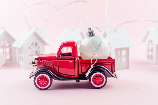 Pickup retrô vermelha com bola de decoração de Natal em fundo rosa pastel.