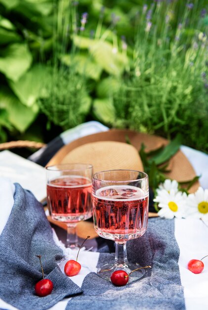 Picnic al aire libre en campos de lavanda. Vino rosado en una copa, cerezas y sombrero de paja sobre una manta