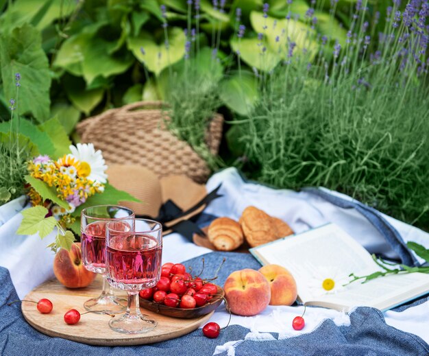 Picnic al aire libre en campos de lavanda. Vino rosado en una copa, cerezas y sombrero de paja sobre una manta