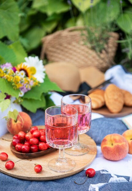 Picnic al aire libre en campos de lavanda. Vino rosado en una copa, cerezas y sombrero de paja sobre una manta