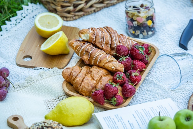 Picnic al aire libre en un exuberante parque verde con un sabroso croissant, rosquillas de frutas y vino sobre el césped