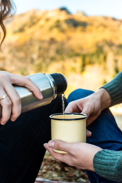 Picnic en el bosque de otoño. manos femeninas vierten té de un termo en una taza retro. paseo romántico otoño