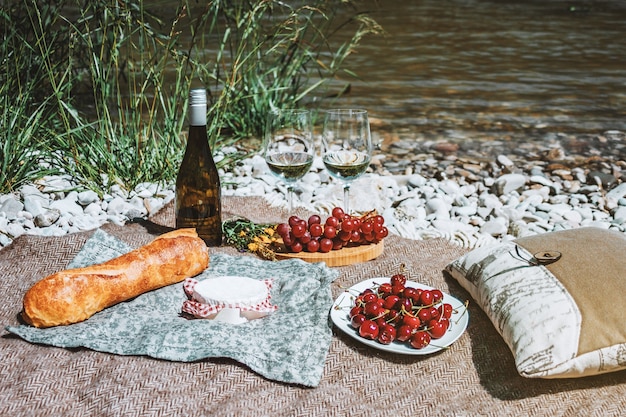 Picnic en la costa con copas de vino blanco botella baguette cerezas queso uva libro abierto