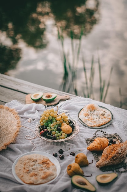 Picnic en estilo antiguo, frutas y pan con platos antiguos, decoraciones en una espalda de madera cerca del agua