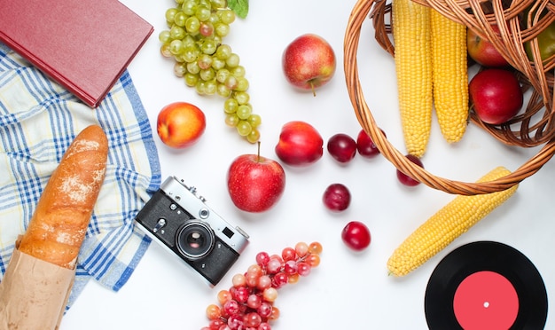 Picnic de estilo retro francés. Cesta con frutas y verduras, cámara retro, libro, baguette y otro fondo blanco de comida de picnic.