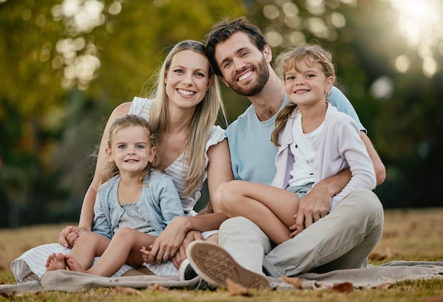 Picnic familiar en el parque y retrato con sonrisa amor y felicidad por unirse en la hierba y el sol Césped familiar joven feliz y padres con árboles para niños y relajarse juntos para las vacaciones de verano