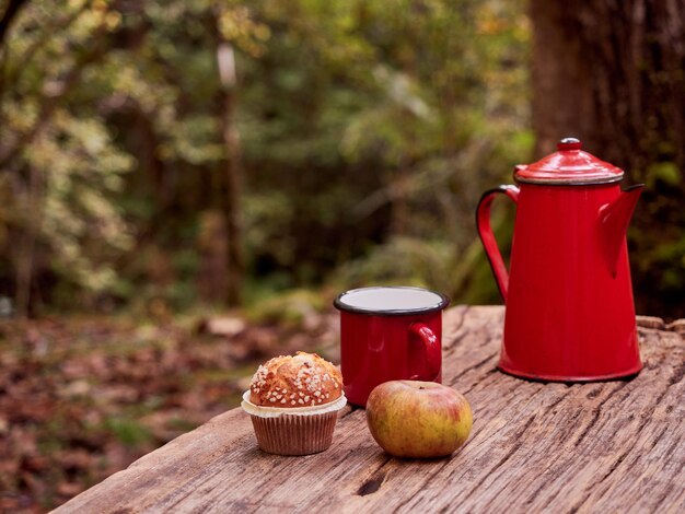 Foto picnic de invierno en el bosque cafetera y taza de café vintage roja cupcake y manzana en una mesa de madera