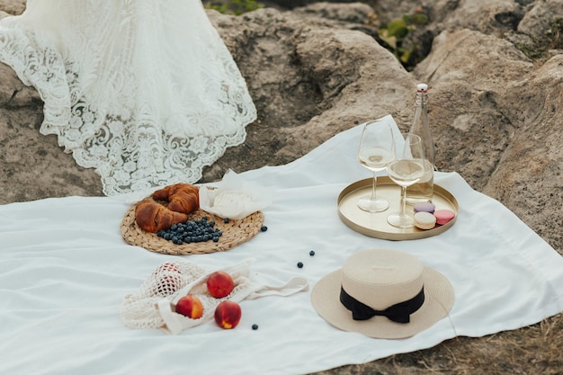 Un picnic con una manta blanca, frutas frescas, un vestido blanco y un sombrero de paja.