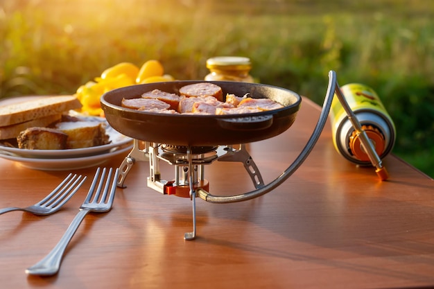 Picnic en la naturaleza salchicha frita en una sartén para acampar