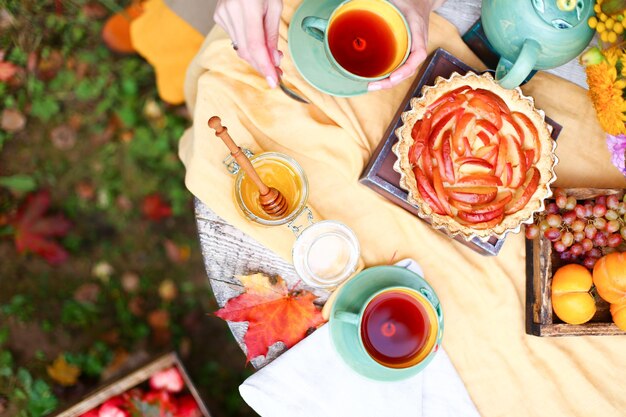 Picnic de otoño Fiesta del té con hermosas tazas de tetera en la mesa de madera en el jardín Festival de la cosecha Miel con cuchara de palo Tarta de manzana Caquis uvas Flores de hoja de arce Mantel de lino amarillo