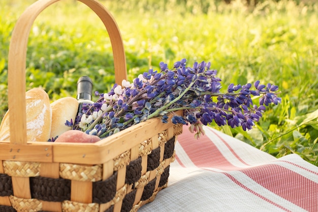 Picnic romántico para una pareja Cesta con flores vino melocotones y baguettes