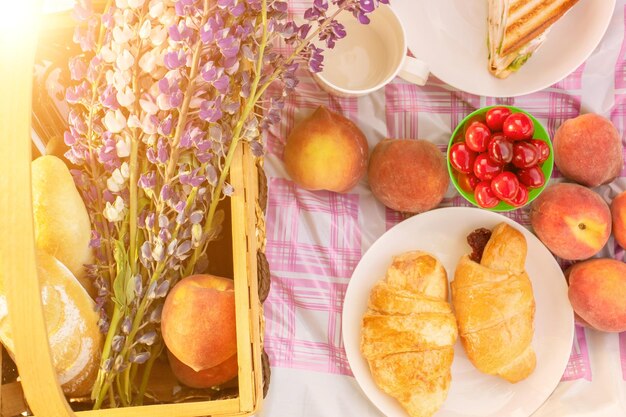 Picnic romántico para una pareja Cesta con flores vino melocotones sándwiches en el mantel