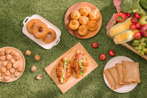 Picnic saludable para unas vacaciones de verano con croissants recién horneados, fruta fresca y ensalada de frutas, sándwiches y un vaso de jugo de naranja refrescante sobre un paño y una cesta a cuadros rojos y blancos.