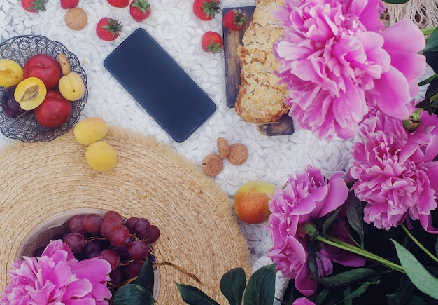 Picnic de verano al aire libre al estilo francés con croissant de almendras y frutas frescas y flores de peonía
