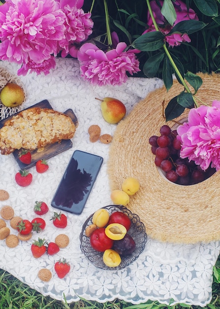 Picnic de verano al aire libre al estilo francés en un jardín de peonías con croissant de almendras y frutas frescas