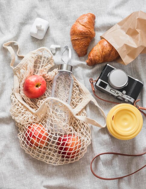 Picnic de verano lugar croissants fruta cámara café en una termotaza en una vista superior de manta gris