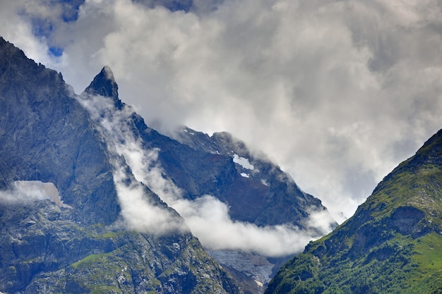 Pico da montanha com geleiras contra o fundo das nuvens e do céu