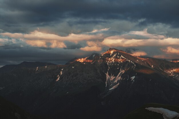 Foto pico de montanha paisagem por do sol com sombrio dramático céu principalmente nublado e raios de sol laranja e vermelho