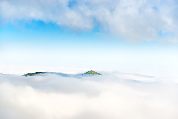 Pico de montanha verde no oceano de nuvens