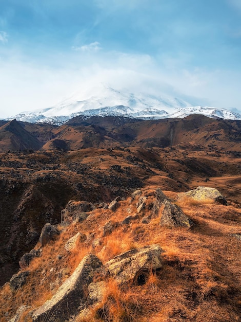 Pico nevado branco brilhante do Monte Elbrus acima do planalto rochoso do outono Outono Elbrus Outono nas montanhas do Cáucaso Neve branca grandes montanhas Picos de neve Visão vertical