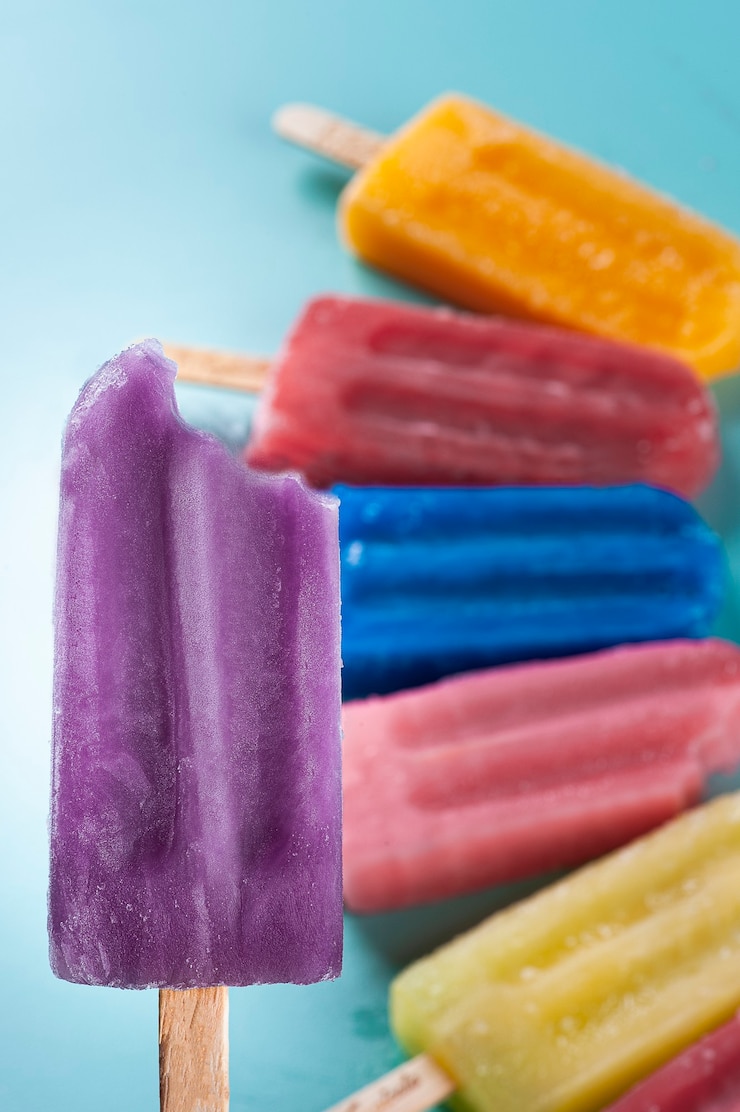 Foto picolé de uva com destaque para vários picolés de sabores variados juntos em um fundo azul