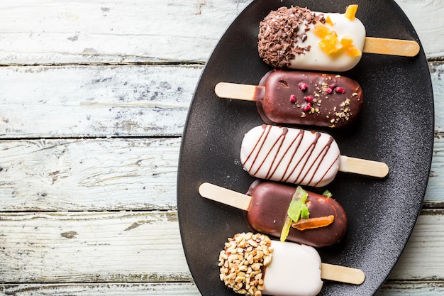 Picolés de baunilha com cobertura de chocolate e cobertura com nozes de amêndoa e doces no fundo branco.