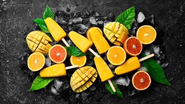 Picolés de frutas tropicais no gelo Doces frios de frutas de verão Em um fundo de pedra preta Vista superior