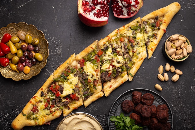 Pide de pizza tradicional turca recién horneada con carne molida y verduras servido sobre fondo de piedra negra con una variedad de meze del Medio Oriente desde arriba, cocina de Turquía