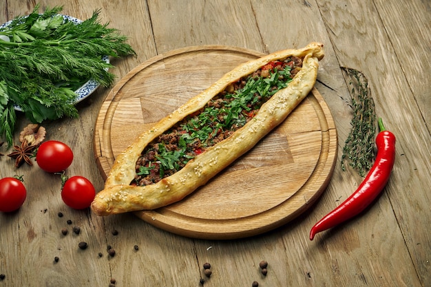 Pide - Türkisches Gericht in Form einer Tortilla mit Rind- oder Lammhackfleisch und Frühlingszwiebeln auf einem Holztablett. Orientalische Pizza, Rezept oder Menü