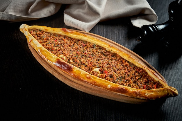 Pide turca com cordeiro picado, tomate e pimentão em uma mesa preta