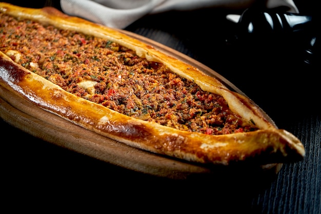 Pide turco con cordero picado, tomate, pimiento servido en bandeja de madera. mesa negra