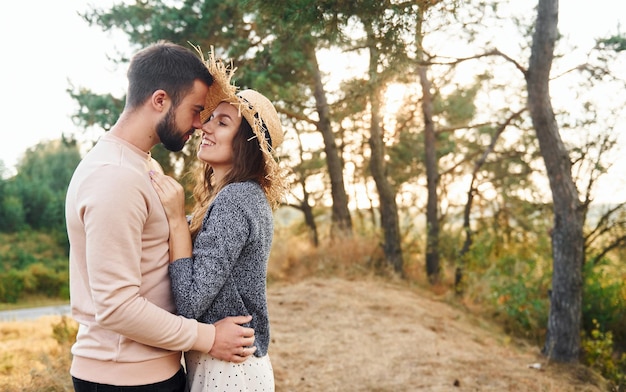 De pie y abrazando a una alegre y encantadora pareja joven descansando juntos al aire libre