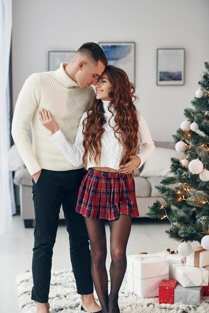 De pie cerca de abeto Joven pareja romántica celebra el Año Nuevo juntos en el interior