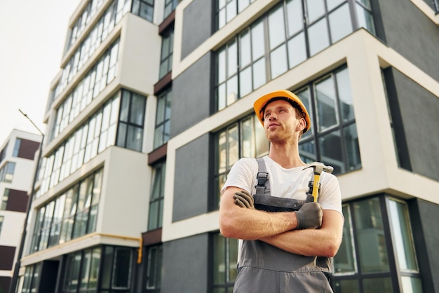 De pie cerca de edificios modernos Joven trabajando en uniforme en la construcción durante el día