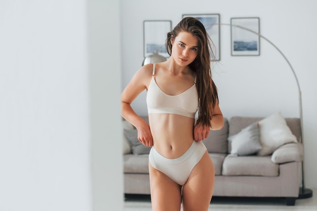 Foto de pie contra el sofá hermosa mujer en ropa interior está posando en el interior