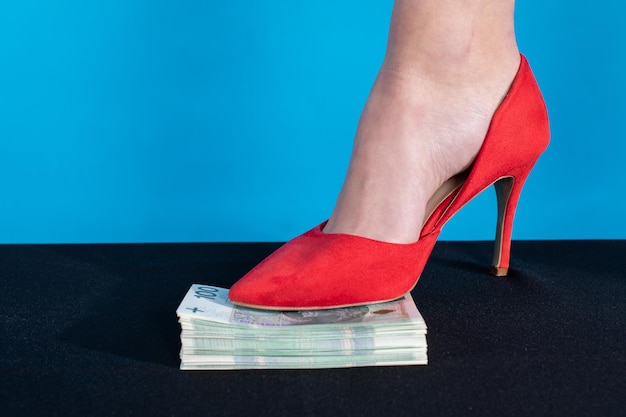 Foto un pie femenino en un tacón alto rojo presiona un paquete de dinero