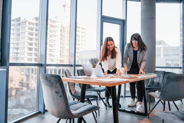 De pie y hablando Dos mujeres vestidas formalmente están adentro en la oficina moderna trabajando juntas