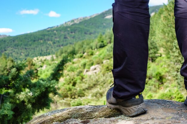 Pie de un hombre escalando una roca y viendo el paisaje montañoso