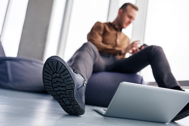 El pie de un hombre con zapatos está cerca de la computadora portátil. El hombre quiere pisar su computadora portátil