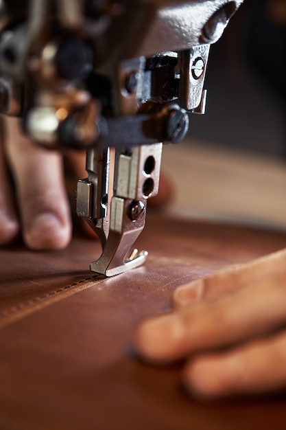 Un pie de máquina de coser con las manos de un maestro de cerca, un sastre hace una costura en una pieza de cuero en una máquina de coser, el concepto de coser productos de cuero.