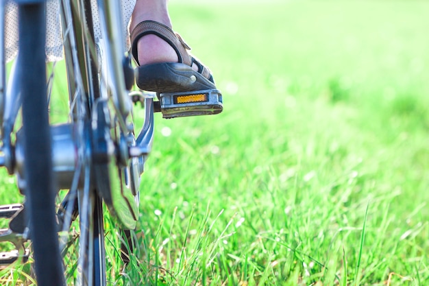 Pie de mujer en pedal de bicicleta en primer plano de hierba verde