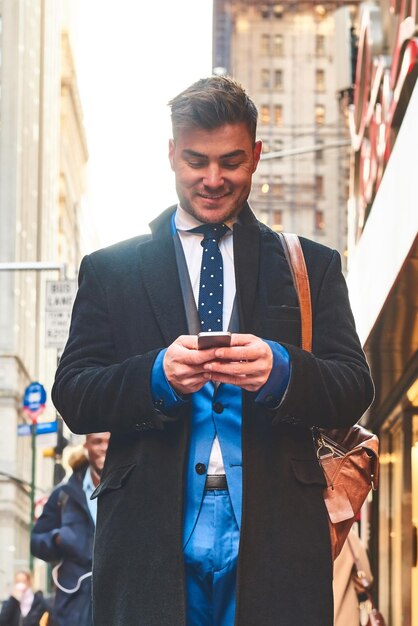 De pie solo en un mundo diferente Foto de un joven alegre que envía mensajes de texto a su teléfono celular mientras está de pie en las concurridas calles de la ciudad durante el día